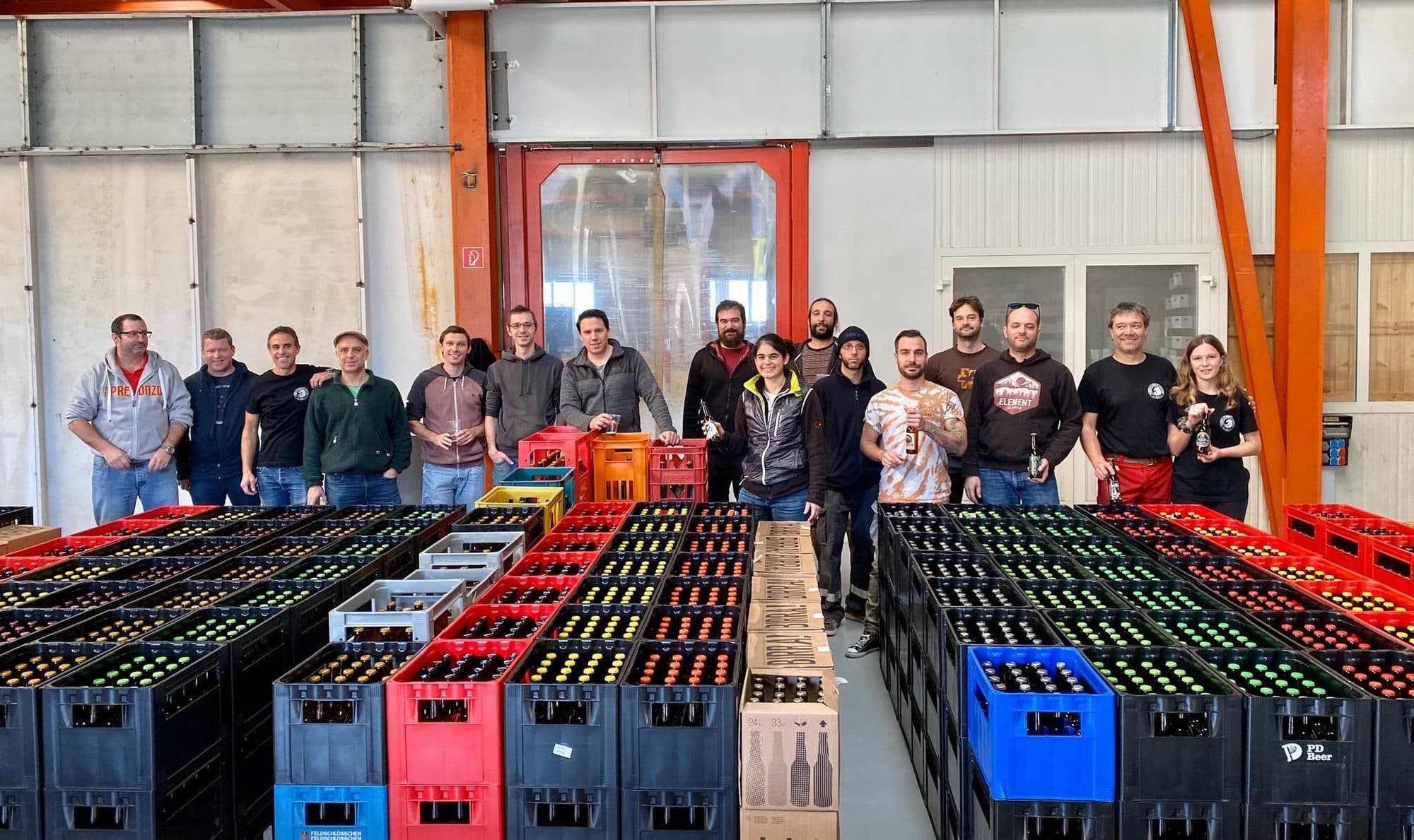 Foto di gruppo dell'edizione 2019: i birrai in posa dietro alle casse di bottiglie allineate sul pavimento del capannone.